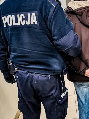 policjant trzyma zatrzymanego ubranego w brązową kutkę