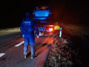 policjant nocą stoi na drodze, przed nim samochód koloru srebrnego na lawecie