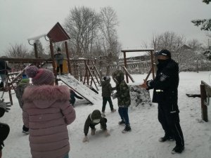 policjant stoi na placu zabaw, obok niego grupa dzieci bawiących się śniegiem
