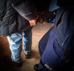 policjant nakłada zatrzymanemu mężczyźnie kajdanki na ręce trzymane z tyłu