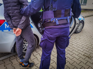 policjant trzyma zatrzymanego mężczyznę.