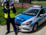 policjant stoi przy radiowozie, w ręku trzyma urządzenie do pomiaru prędkości pojazdów