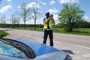 policjant w żółtej kamizelce mierzy przy drodze prędkość