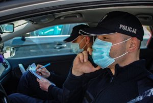 policjanci siedzą w radiowozie, mają założone maseczki na twarzy