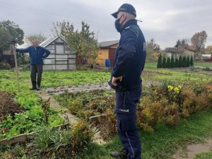 policjant idzie wśród ogródków działkowych