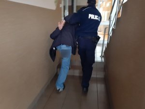 policjant prowadzi mężczyznę, który ma założone kajdanki na rękach