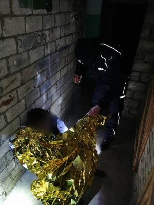 policjant przykrywa folią termiczną siedzącego mężczyznę