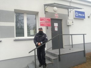 policjant stoi na schodach przed budynkiem. Po prawej stronie budynku napis Policja