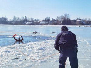 policjant wyciagą liną osobę z zamrznietego zbiornika wodnego