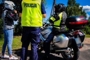 policjant stoi przy dwójce motocyklistów, obok motocykl