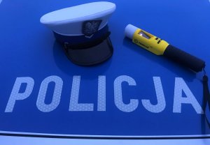 na masce radiowozu napis POLICJA, obok czapka policjanta oraz urządzenie do badania stanu trzeźwości