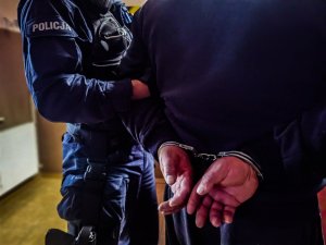 policjant trzyma mężczyznę, który ma założone kajdanki na ręce trzymane z tyłu