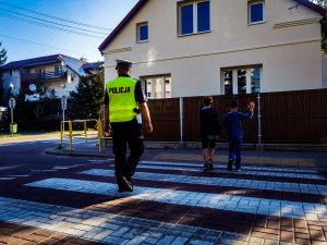 policjant uczy przechodzić dzieci przez przejście dla pieszych