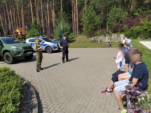 policjant wspólnie z strażnikiem granicznym stoi przed grupą dzieci. W tle radiowozy