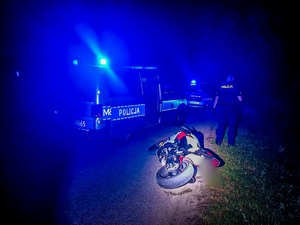 na ziemi lezy przewrócony motocykl, obok radiowozy i policjant